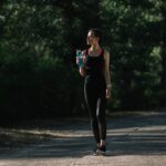 athletic girl holding sports bottle with water and walking in park