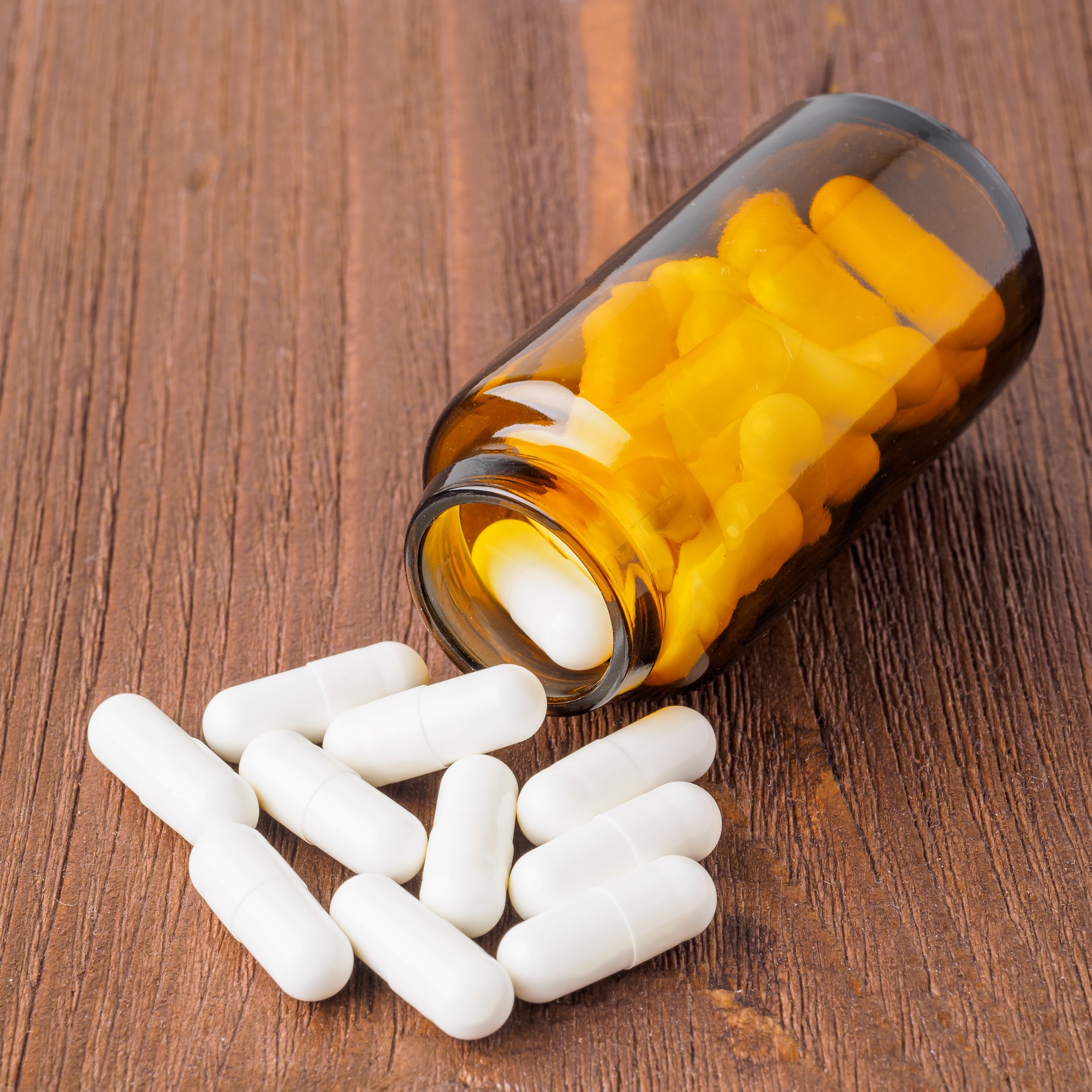 Glass open container with a medicament, jar with pills on brown wooden background