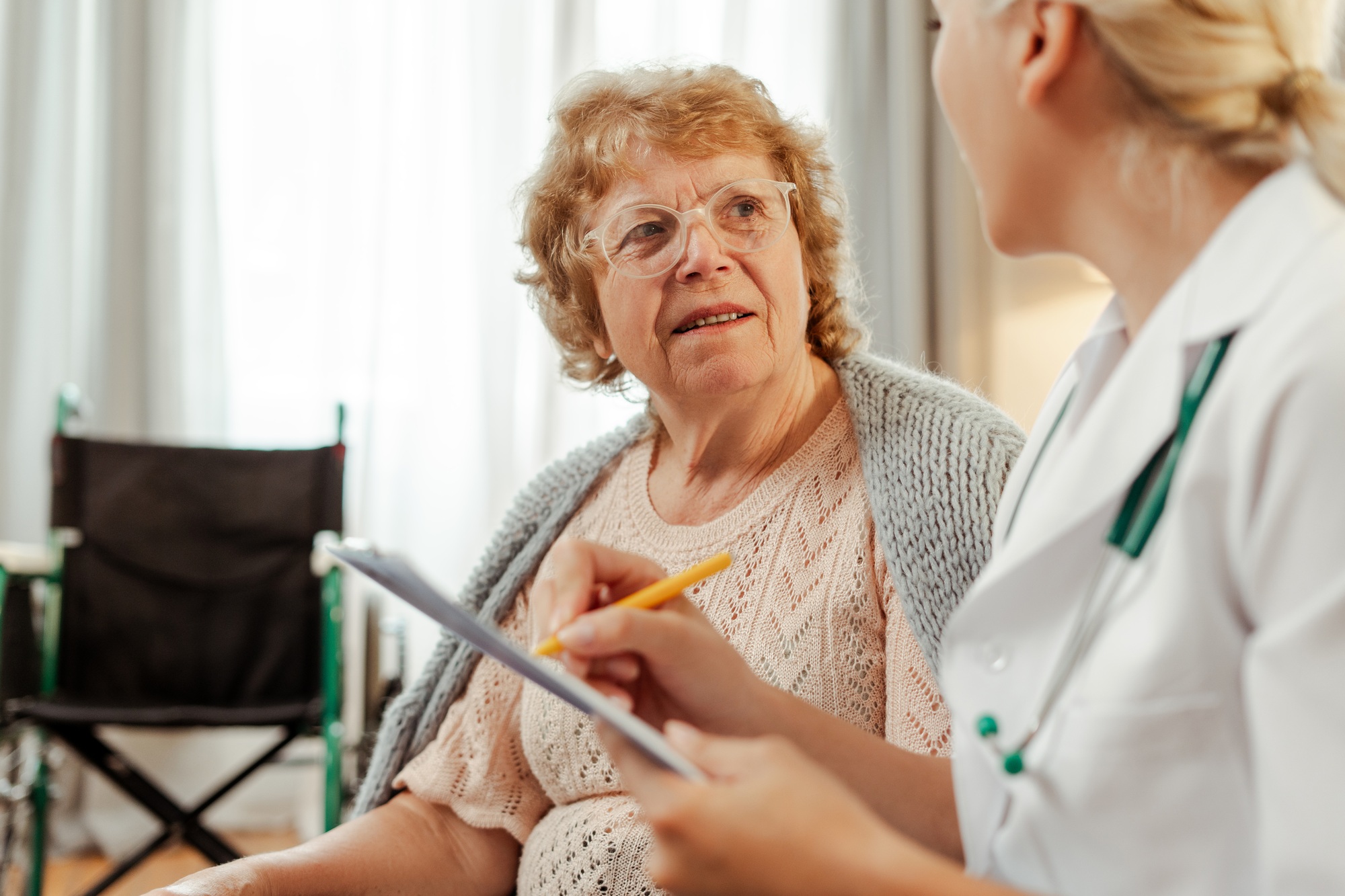 Senior woman signing medical form with doctor at home in living room, health care concept