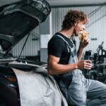 Eats banana and drinks water. Adult man in grey colored uniform works in the automobile salon