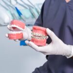 Crop anonymous stomatologist with dentures sitting in clinic